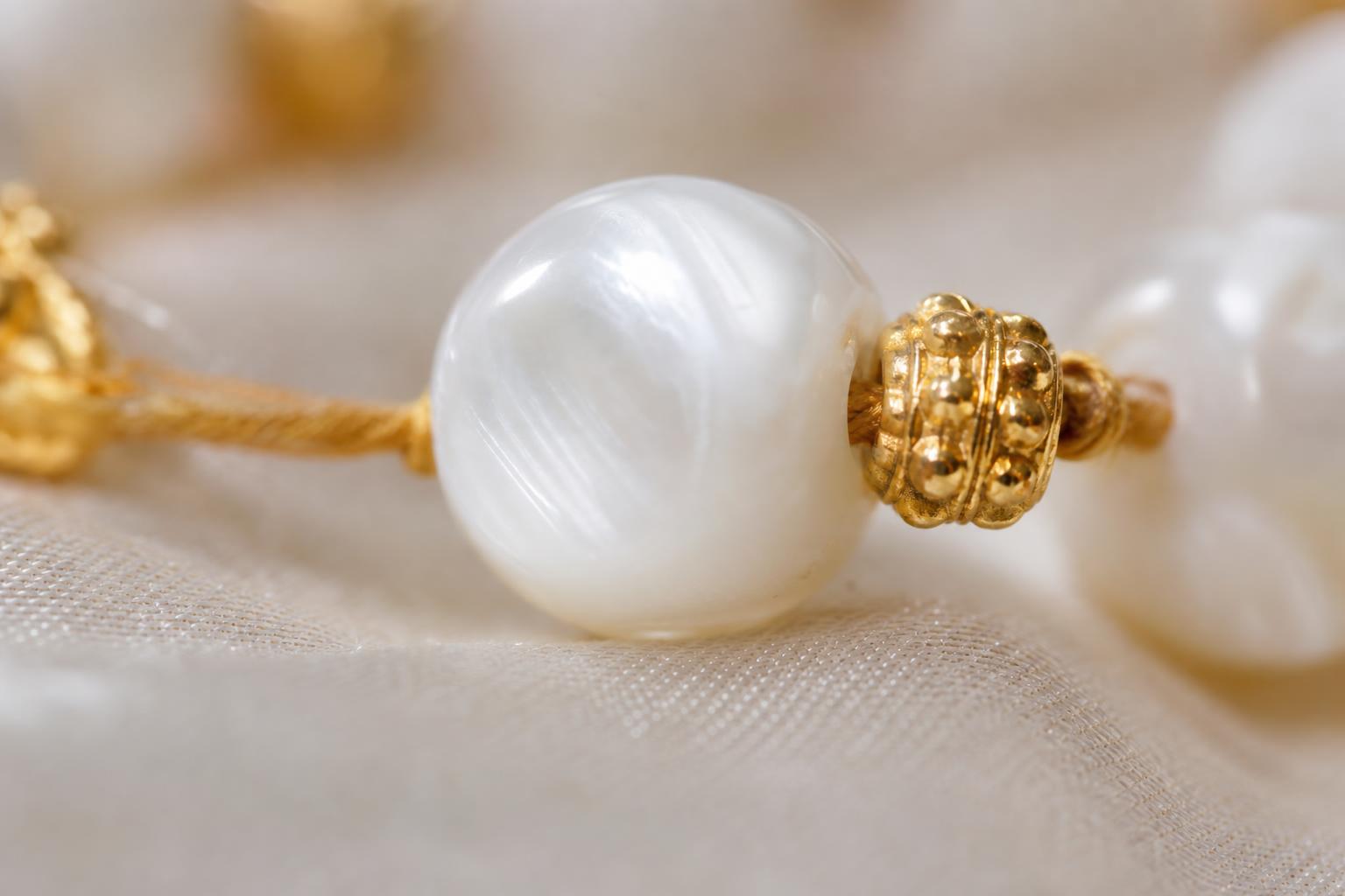 Macro close-up of a luminous white mother-of-pearl tasbih bead next to a gold spacer bead on cream silk
